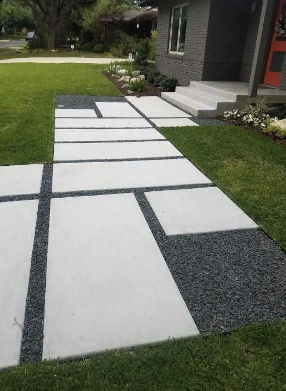 Large rectangular concrete slabs set in dark gravel, forming a walkway to front porch steps